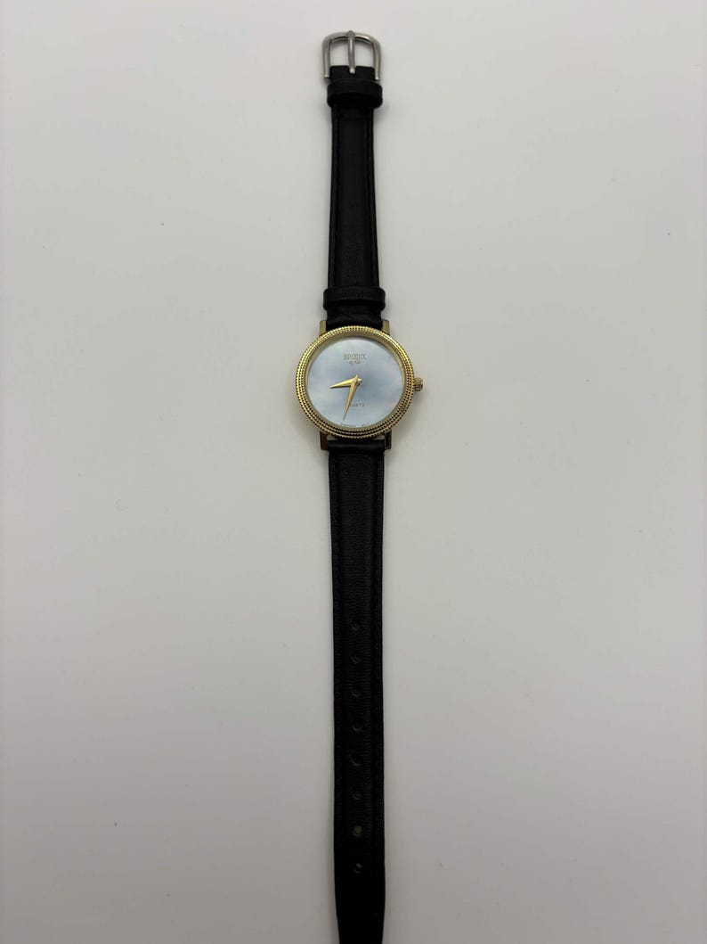 May include: A gold-toned wristwatch with a light blue face and black leather band. The watch has gold hands and a gold bezel. The watch band is thin and has a silver buckle. The watch is centered on a white background.