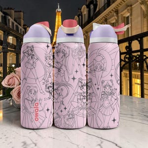 May include: Three pink Owala water bottles with black and white anime character illustrations. Each bottle has a light purple lid with a pink flip-top and a white handle. The background features a Parisian street scene.