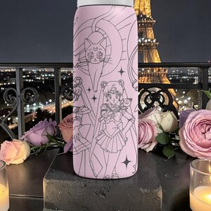 May include: A pink water bottle featuring a black line art design of anime characters and a cat. The bottle is cylindrical with a white lid. The background includes roses, candles, and a city skyline.