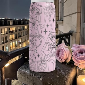May include: A pink water bottle featuring a black line art design of anime characters and stars. The bottle is cylindrical and appears to be made of metal. The background includes a balcony, roses, and a candle.