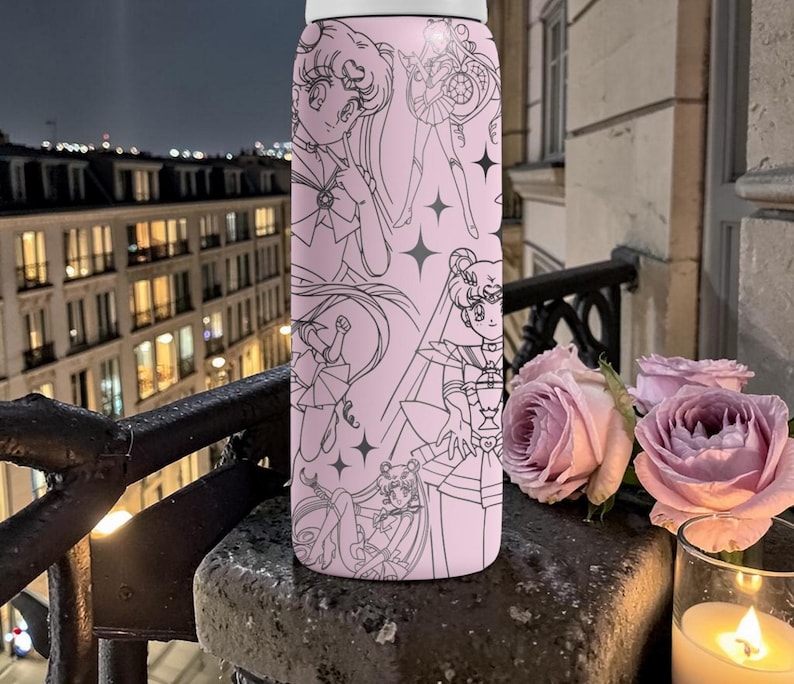 May include: A pink water bottle featuring a black line art design of anime characters and stars. The bottle is cylindrical and appears to be made of metal. The background includes a balcony, roses, and a candle.