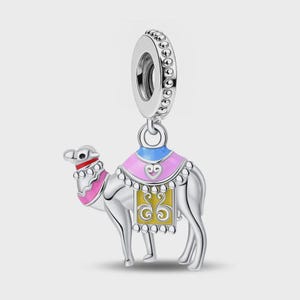 Puede incluir: Un charm de plata con forma de camello que presenta detalles en esmalte de colores. El camello tiene un collar rosa, una silla de montar rosa y azul con un detalle de corazón y un panel lateral rectangular amarillo con adornos plateados.