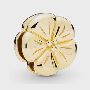 May include: A polished gold-tone charm shaped like a five-petaled flower. The charm features smooth, rounded petals with subtle engraved lines radiating from the centre, which is accented by three small, raised spherical beads in a cluster.