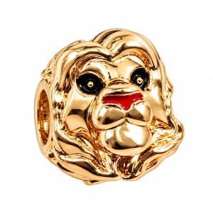 May include: A gold-toned metal charm shaped like a lion head with a flowing mane. The lion features glossy black enamel eyes with small gold centres and a bright red enamel nose. The charm has a hollow centre for threading onto a bracelet.