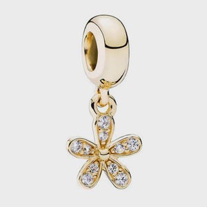 Könnte beinhalten: Ein goldfarbener Anhänger mit einer glatten, abgerundeten Öse, die an einem fünfblättrigen Blumenanhänger befestigt ist. Die Blume besteht aus poliertem, goldfarbenem Metall und ist mit kleinen, klaren, funkelnden Steinen auf jedem Blütenblatt besetzt.