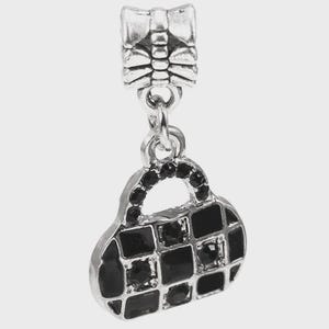 May include: A silver-toned metal charm featuring a bow-shaped bail attached to a handbag-shaped pendant. The handbag pendant has a grid pattern filled with black enamel and small, round, black sparkling stones set within the grid squares.