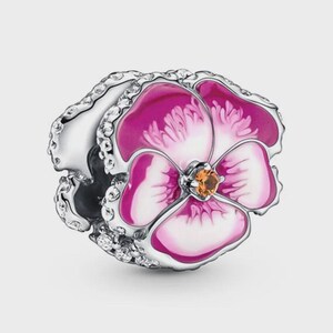 May include: A silver charm bead shaped like a pansy flower, featuring vibrant pink and white enamel petals. The centre of the flower is accented with a small, round orange stone, and the outer edges of the silver frame are set with clear, sparkling stones.