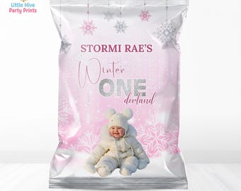 May include: A pink and silver party favor bag with the text "STORMI RAE'S Winter ONE derland". The bag features a baby in a white snowsuit and snowflakes. The text "Editable in Canva . Instant Download" is at the bottom.