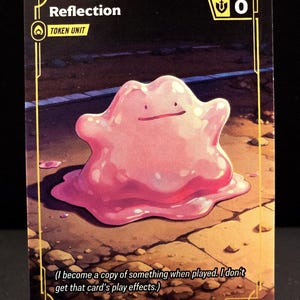 Puede incluir: Una carta coleccionable con un personaje rosa amorfo llamado "Reflection". La tarjeta tiene un borde dorado y el texto "TOKEN UNIT" y "0". La parte inferior de la tarjeta dice: "(Me convierto en una copia de algo cuando se juega. No obtengo los efectos de juego de esa carta.)"