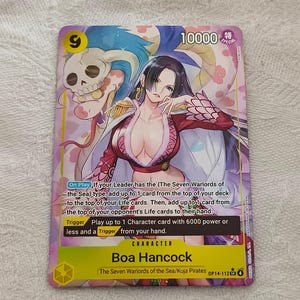 Könnte beinhalten: Sammelkarte mit Boa Hancock aus der One Piece-Serie. Die Karte zeigt eine farbenfrohe Illustration der Figur, Text und eine Stärke von 10000. Die Karte liegt auf einer weißen Oberfläche.