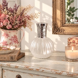 May include: A frosted glass fragrance lamp with a rounded, ribbed body and a silver-toned metal crown top. The lamp features a translucent finish and a wide base, designed to hold a wick and fragrance oil for home scenting purposes.