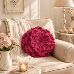 Peut inclure: Un coussin rond de couleur magenta profond doté d'une construction en tissu à pétales superposés imitant l'apparence d'une fleur en pleine floraison. Le coussin présente un centre dense et texturé entouré de rangées de pétales souples.