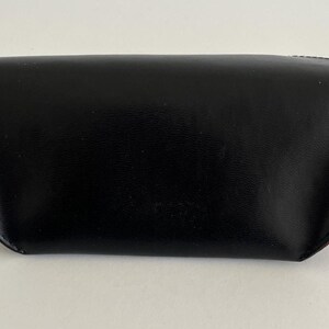 Puede incluir: Un estuche para gafas negro, de aspecto cuero, con forma curvada. El estuche tiene un acabado liso y brillante y un acento rojo en el lateral. El estuche est&aacute; cerrado y parece estar vac&iacute;o.