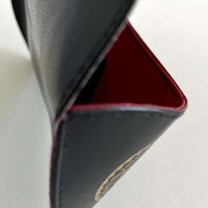 Puede incluir: Estuche de cuero negro con interior rojo. El estuche est&aacute; abierto, revelando el forro rojo y un vistazo a un emblema dorado. Los bordes est&aacute;n cuidadosamente cosidos y el estuche parece estar hecho de materiales de alta calidad.