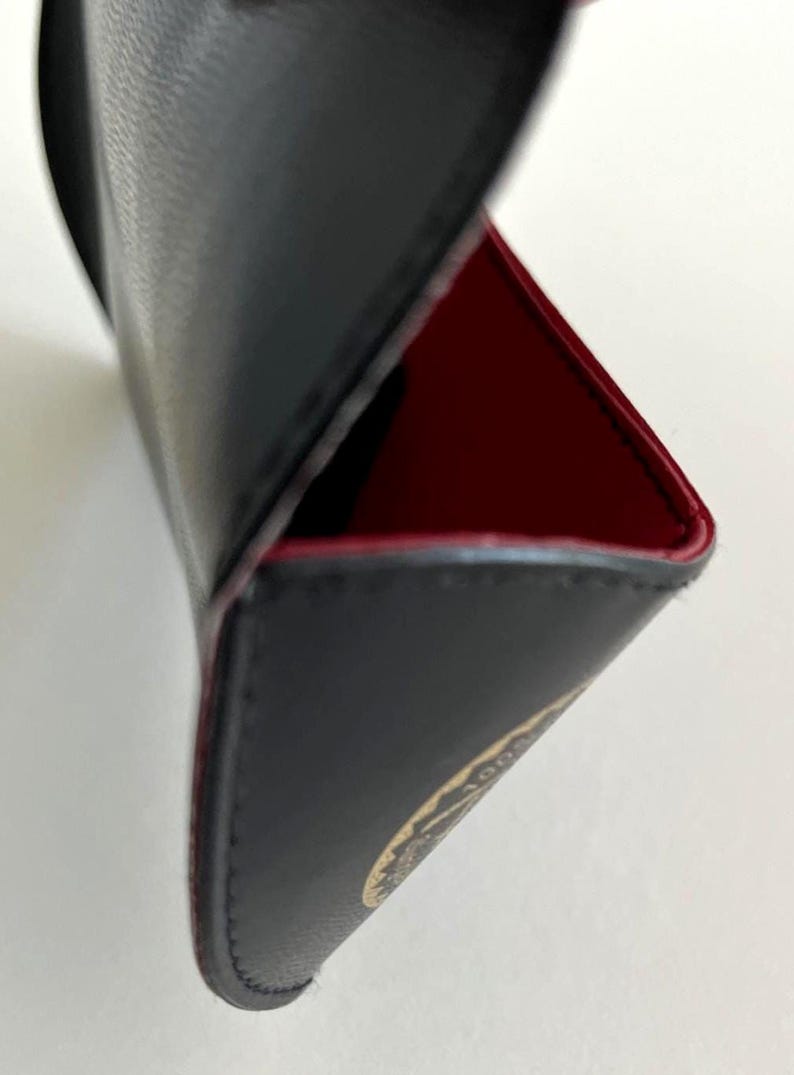 Puede incluir: Estuche de cuero negro con interior rojo. El estuche est&aacute; abierto, revelando el forro rojo y un vistazo a un emblema dorado. Los bordes est&aacute;n cuidadosamente cosidos y el estuche parece estar hecho de materiales de alta calidad.