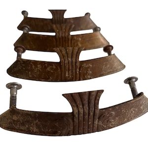 Peut inclure: Un ensemble de quatre poignées de tiroir en métal assorties avec une finition bronze patiné. Chaque poignée présente une forme incurvée et allongée avec un détail central nervuré vertical et deux boulons filetés à l'arrière pour la fixation.