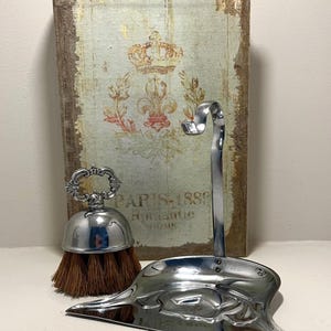 Peut inclure: Un ensemble ramasse-miettes en métal argenté composé d'une brosse à main avec une poignée décorative et d'une pelle assortie dotée d'un long manche incurvé. La brosse présente des poils bruns et une finition métallique polie et brillante.
