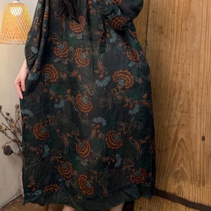 May include: Dark green, long-sleeve dress with a floral paisley pattern in shades of orange and blue. The dress has a loose, flowing silhouette and a round neckline. The dress is paired with brown slip-on shoes.