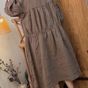 May include: A brown linen dress with a tiered design and long sleeves. The dress has a relaxed fit and falls to the mid-calf. The dress is made of a lightweight fabric and has a simple, elegant style.