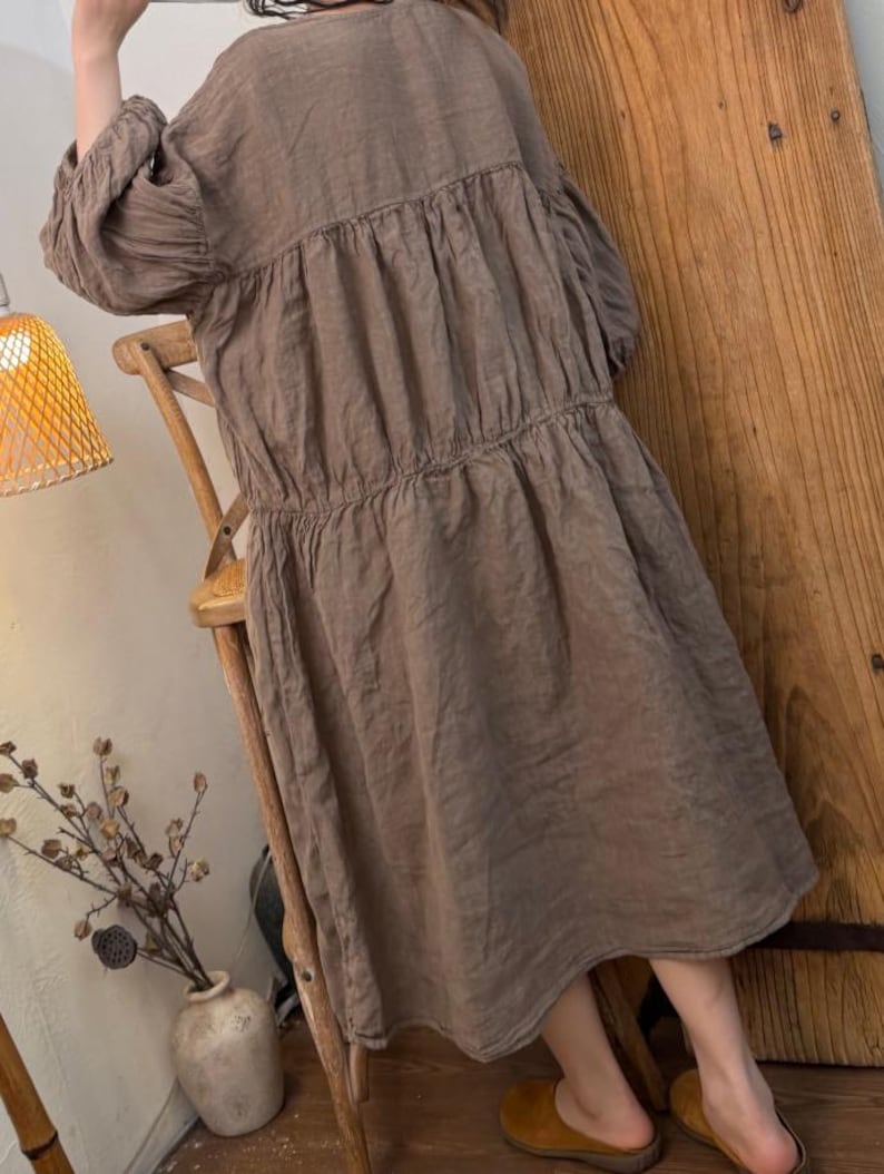 May include: A brown linen dress with a tiered design and long sleeves. The dress has a relaxed fit and falls to the mid-calf. The dress is made of a lightweight fabric and has a simple, elegant style.