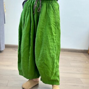 May include: Bright green linen pants with a drawstring waist. The wide-leg pants have a relaxed fit and are made of a textured fabric. The pants are paired with tan colored slippers. The pants are a vibrant shade of green.