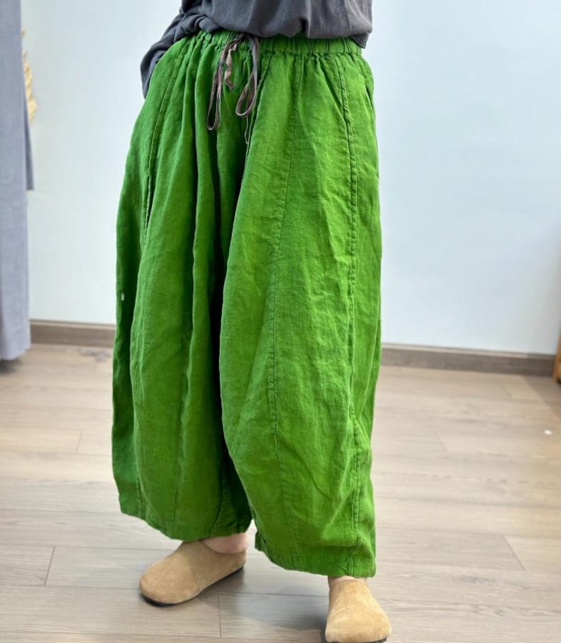 May include: Bright green linen pants with a drawstring waist. The wide-leg pants have a relaxed fit and are made of a textured fabric. The pants are paired with tan colored slippers. The pants are a vibrant shade of green.