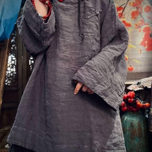 May include: A gray linen tunic with long sleeves and a button closure at the neck. The tunic has a relaxed fit and a slightly A-line shape.