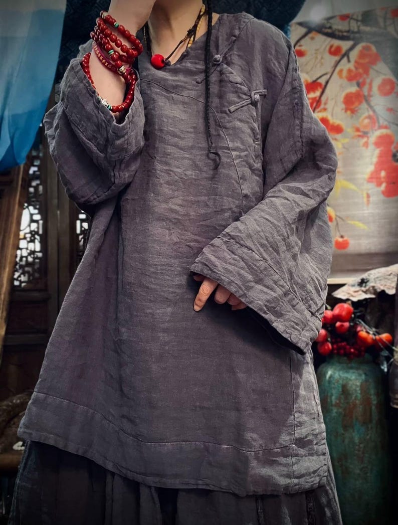 May include: A gray linen tunic with long sleeves and a button closure at the neck. The tunic has a relaxed fit and a slightly A-line shape.