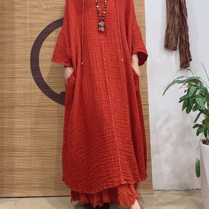 May include: A long, loose-fitting, red linen dress with a hood and pockets. The dress has a simple, casual style and is perfect for warm weather.