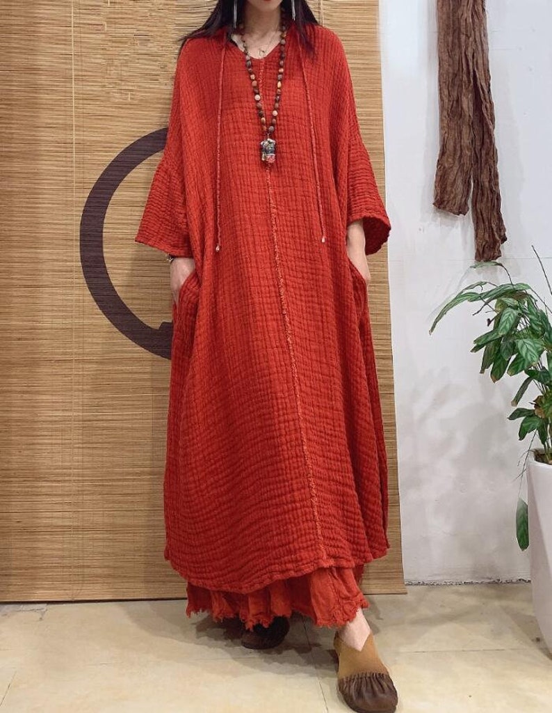 May include: A long, loose-fitting, red linen dress with a hood and pockets. The dress has a simple, casual style and is perfect for warm weather.