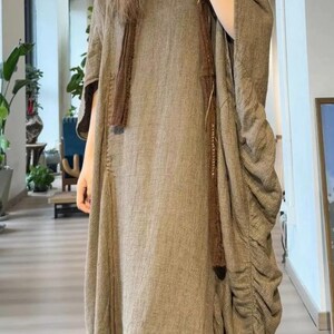 May include: A long, flowing brown dress with a matching scarf. The dress has a loose fit with gathered fabric on the side. The fabric appears to be a textured weave, creating a casual, comfortable look.