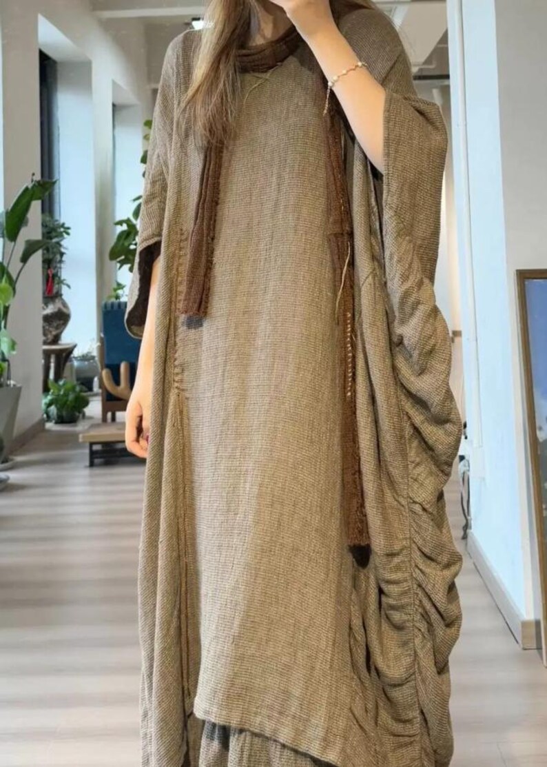 May include: A long, flowing brown dress with a matching scarf. The dress has a loose fit with gathered fabric on the side. The fabric appears to be a textured weave, creating a casual, comfortable look.