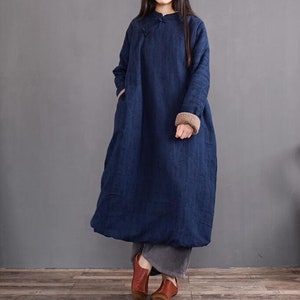 May include: A long, navy blue,  linen dress with a mandarin collar and long sleeves. The sleeves have a brown fleece lining. The dress has a loose, flowing fit.