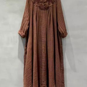 May include: A long, flowing brown dress with a V-neckline and long sleeves. The neckline features intricate floral embroidery. The dress has a loose, comfortable fit, perfect for casual wear. The fabric appears to be a lightweight, textured material.