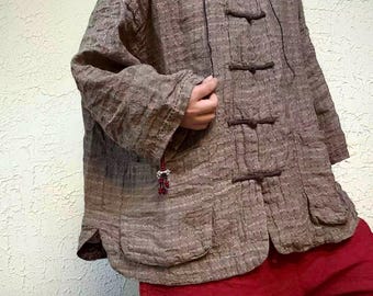 May include: A brown textured long-sleeve jacket with a mandarin collar and four dark brown toggle closures down the front. The jacket features two large patch pockets at the bottom hem and a small decorative red bead charm hanging from the sleeve cuff.