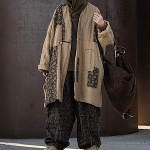 May include: A beige patchwork coat with floral accents and matching pants. The coat has a long, loose fit with dark floral patches. The pants are a dark floral pattern. A brown bag hangs from the shoulder.