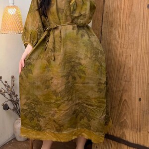 May include: A long, olive green dress with a leaf pattern. The dress has long, puffy sleeves, a round neckline, and a matching belt. The hemline and sleeve cuffs are trimmed with a mustard yellow fabric.
