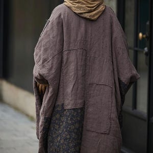 May include: A brown, oversized coat with a hood, featuring patchwork details. The coat has a floral pattern on the lower section and is made of a textured fabric. The hood is a lighter shade of brown.