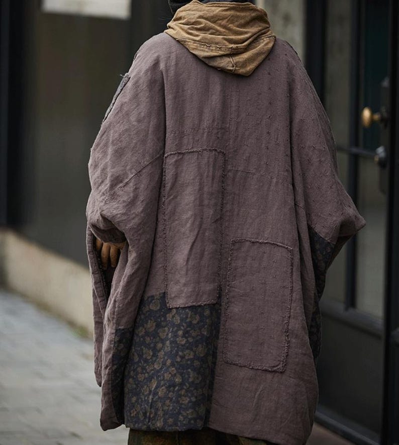 May include: A brown, oversized coat with a hood, featuring patchwork details. The coat has a floral pattern on the lower section and is made of a textured fabric. The hood is a lighter shade of brown.