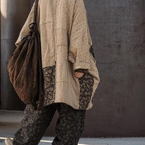 May include: A beige patchwork coat with floral accents and matching pants. The coat has a loose fit and a hood. A large brown drawstring bag is slung over the shoulder. The pants have a dark floral pattern. The outfit is worn with sneakers.