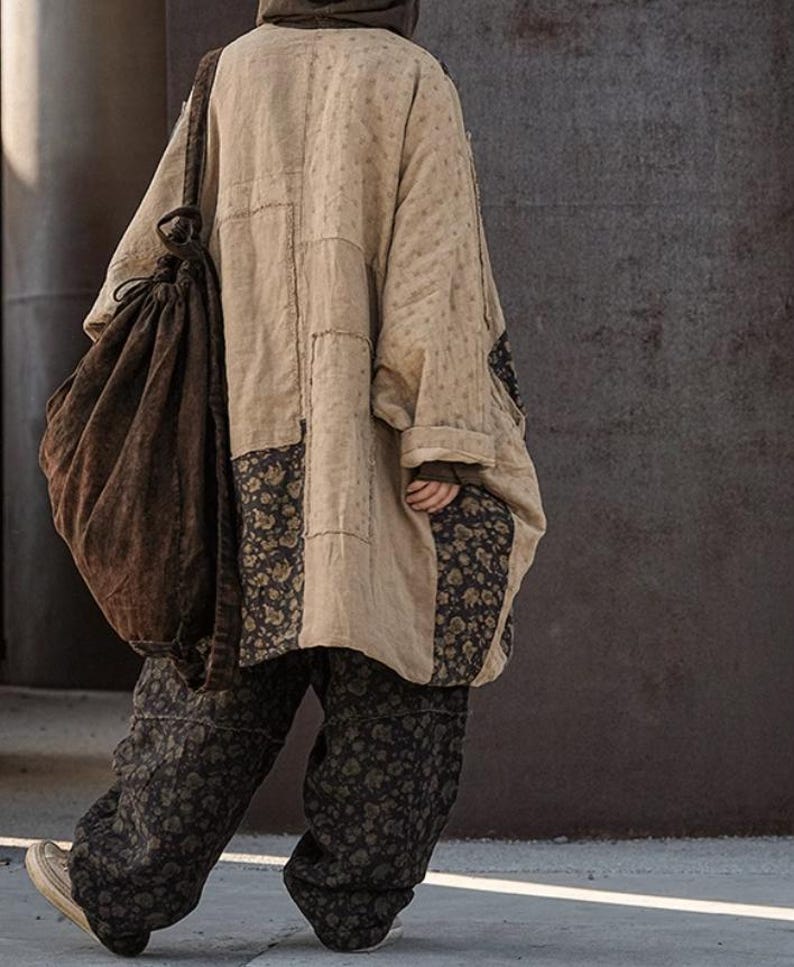 May include: A beige patchwork coat with floral accents and matching pants. The coat has a loose fit and a hood. A large brown drawstring bag is slung over the shoulder. The pants have a dark floral pattern. The outfit is worn with sneakers.