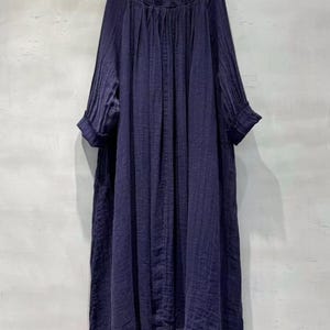 May include: A long, navy blue dress with a floral embroidered neckline. The dress features long sleeves with rolled cuffs and a loose, flowing silhouette. The fabric appears to be a lightweight, textured material.