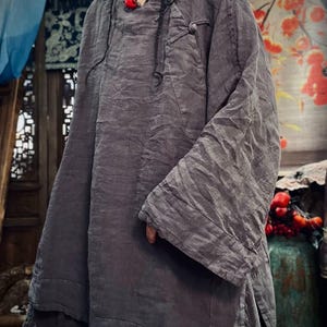 May include: A gray linen tunic with a long, flowing silhouette and a button closure at the neck. The tunic has a relaxed fit and a slightly asymmetrical hemline.