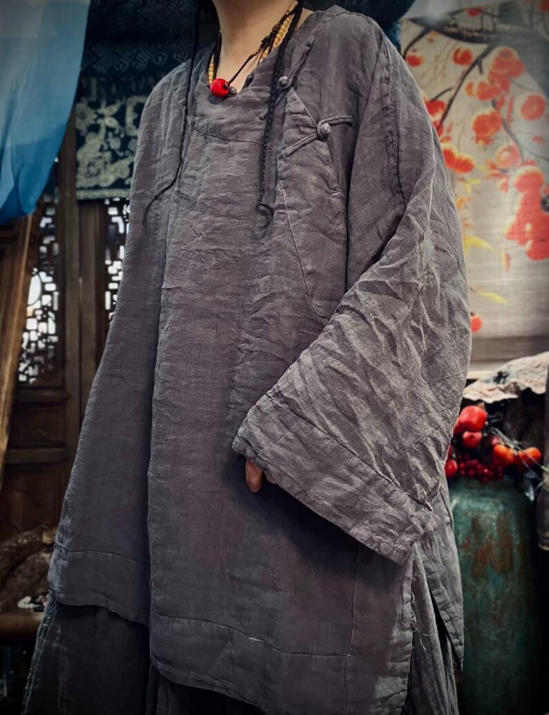 May include: A gray linen tunic with a long, flowing silhouette and a button closure at the neck. The tunic has a relaxed fit and a slightly asymmetrical hemline.