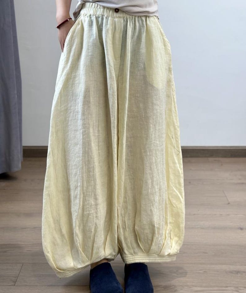 May include: Pale yellow linen pants with a gathered waist and balloon-style legs. The pants have a relaxed fit and pockets. The fabric appears lightweight and breathable, suitable for warm weather. The pants are paired with dark blue socks.