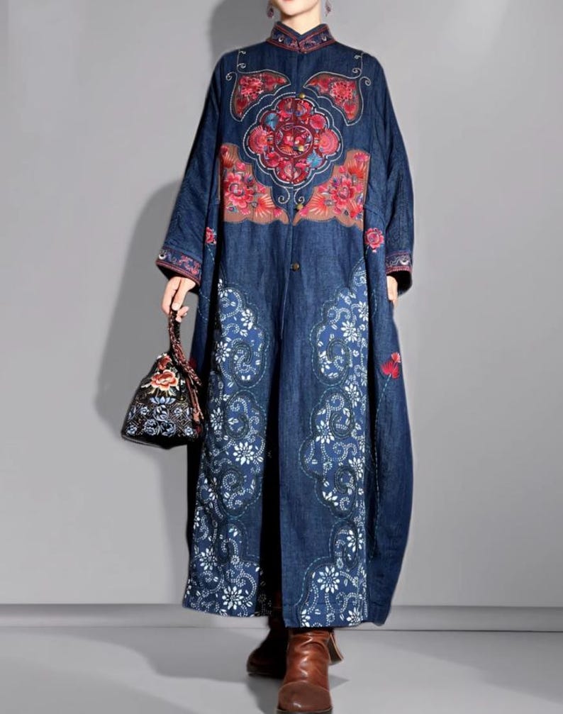May include: A long, dark blue denim coat with intricate floral embroidery in red, pink, and white. The coat features a mandarin collar and a button-down front. A small, patterned handbag complements the outfit. The coat's design is reminiscent of traditional Asian styles.