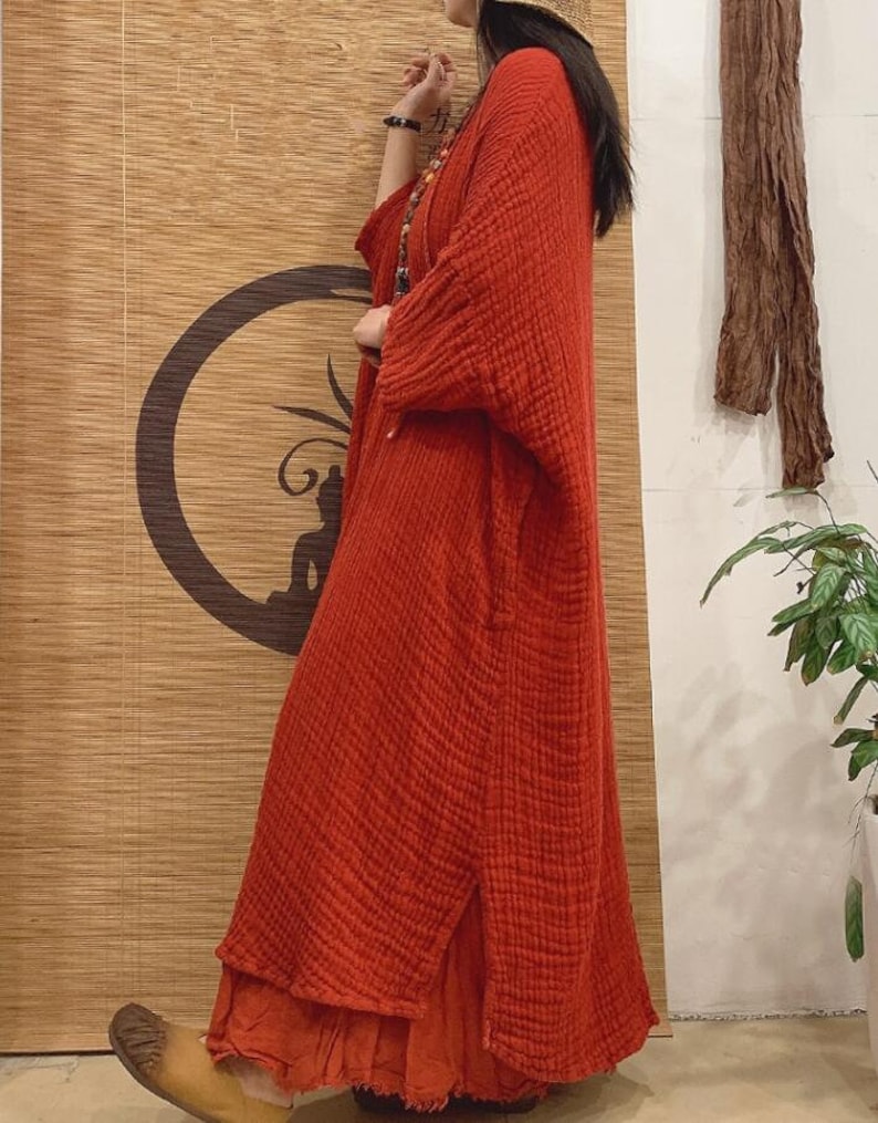 May include: A long, loose-fitting, red linen dress with a side slit and a slightly frayed hem.