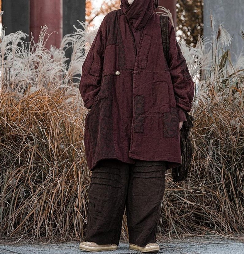 May include: A burgundy-colored, quilted coat with a high collar and a single button closure. The coat has large pockets and is paired with matching dark brown pants. The outfit is worn with tan shoes and a black shoulder bag.