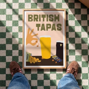 May include: A framed poster with the words "BRITISH TAPAS" in green letters. The poster features illustrations of a pint of beer, a dark stout, a hand gesture, and snacks. The poster is on a green and white checkered floor.