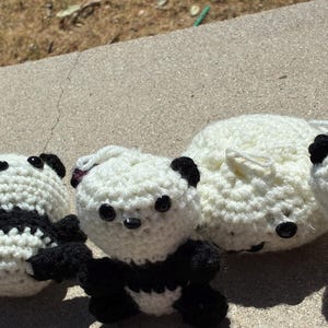 May include: A collection of four small, handmade crochet figures featuring three panda bears with black and white yarn, black plastic eyes, and one solid white round crochet ball, all crafted with a textured, looped stitch pattern.
